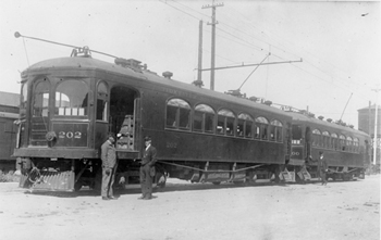Two men standing next to two streetcars in Modesto.